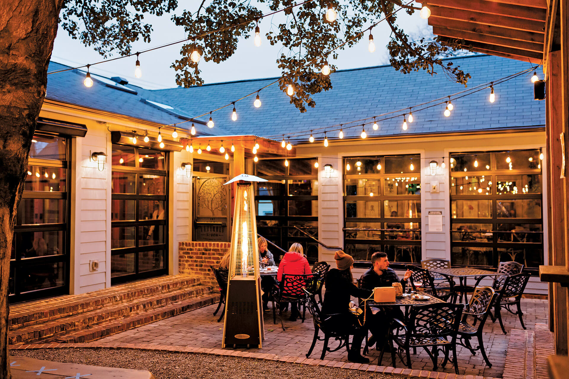 Outdoor dining patio with string lights and guests at The Goodyear House in NoDa Charlotte, photo by Joshua Vasko for Our State Magazine.